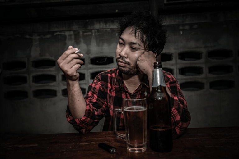 A person sitting at a table with a bottle and a cigarette