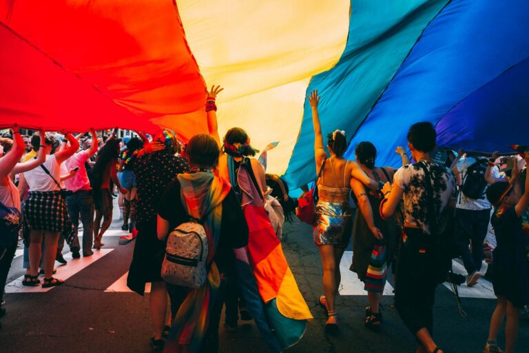 People celebrating under a giant rainbow flag during a Pride parade, symbolizing community and support during Pride Month