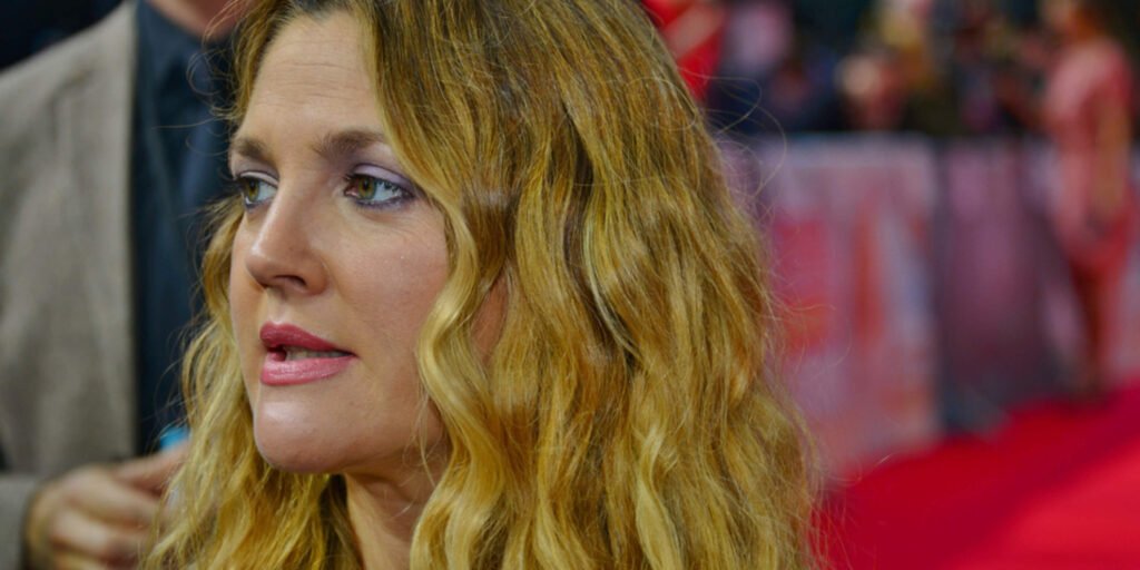 A close-up photograph of actress and producer Drew Barrymore on the red carpet for the movie Blended in Berlin. She has long, wavy blonde hair, light pink lipstick, and soft purple eyeshadow, looking slightly off-camera.