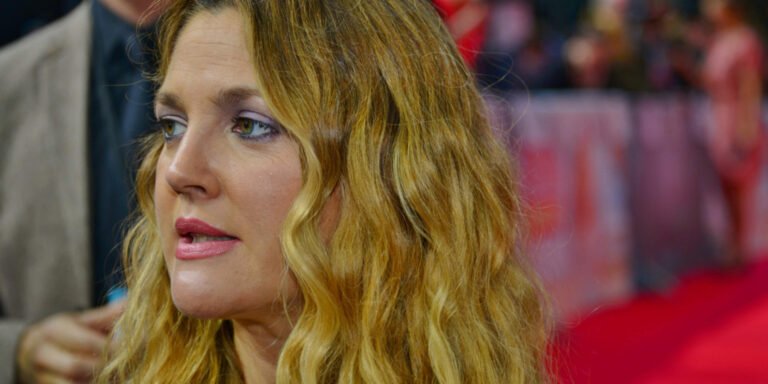 A close-up photograph of actress and producer Drew Barrymore on the red carpet for the movie Blended in Berlin. She has long, wavy blonde hair, light pink lipstick, and soft purple eyeshadow, looking slightly off-camera.