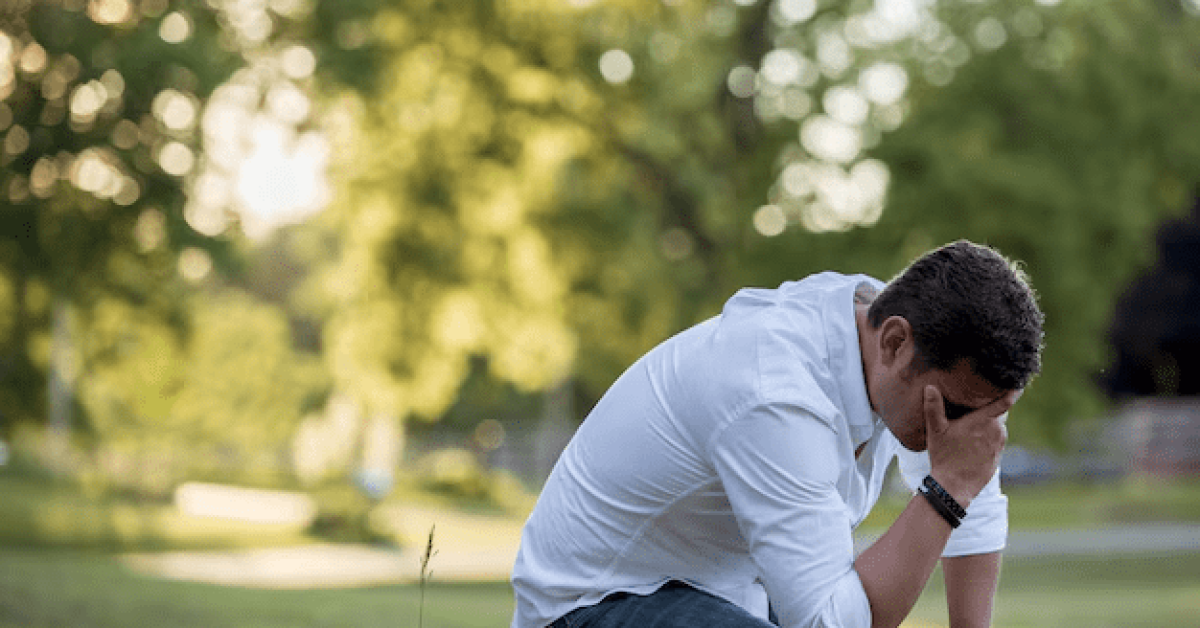 A person struggling with emotional triggers, sitting alone in a park, reflecting on their emotions and seeking coping mechanisms for emotional triggers.