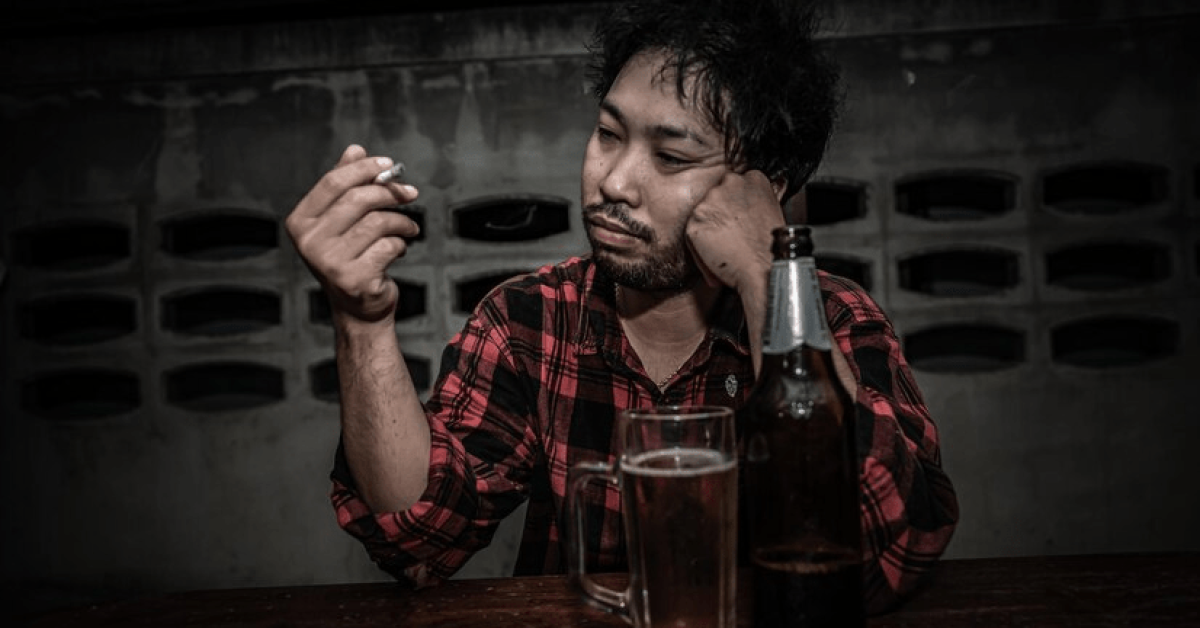 A person sitting at a table with a bottle and a cigarette