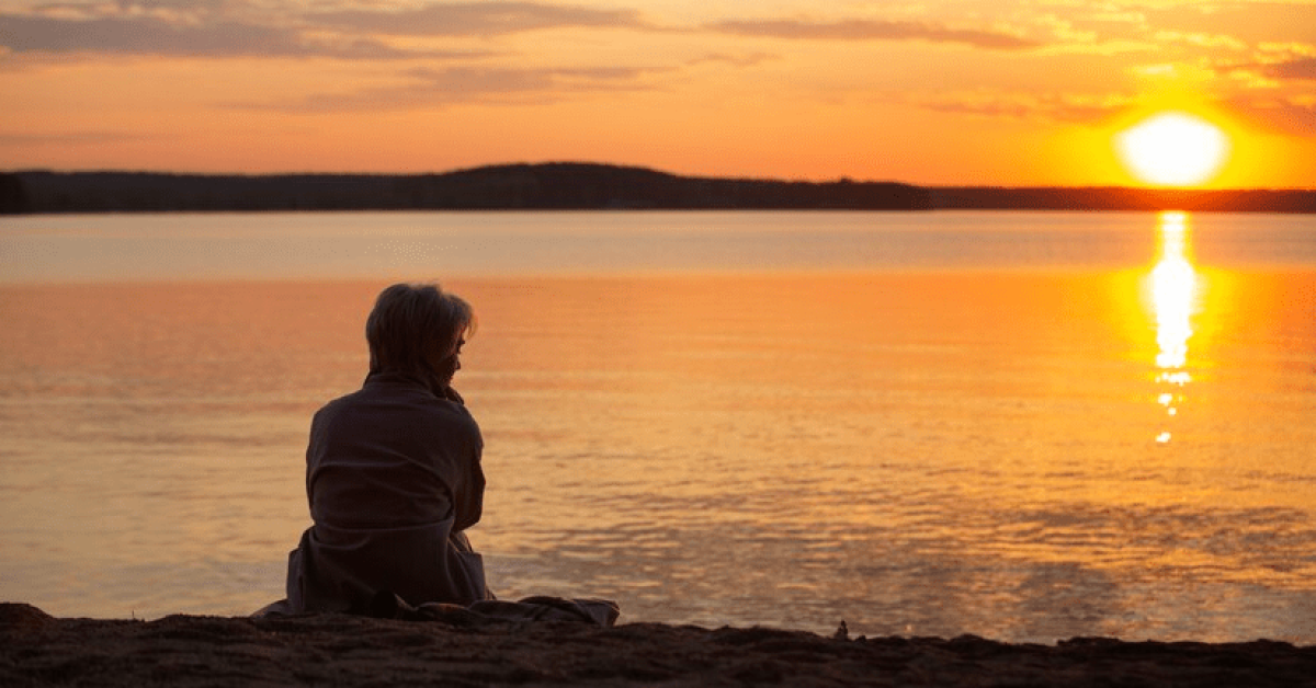 A person sitting on the beach looking at the sunset