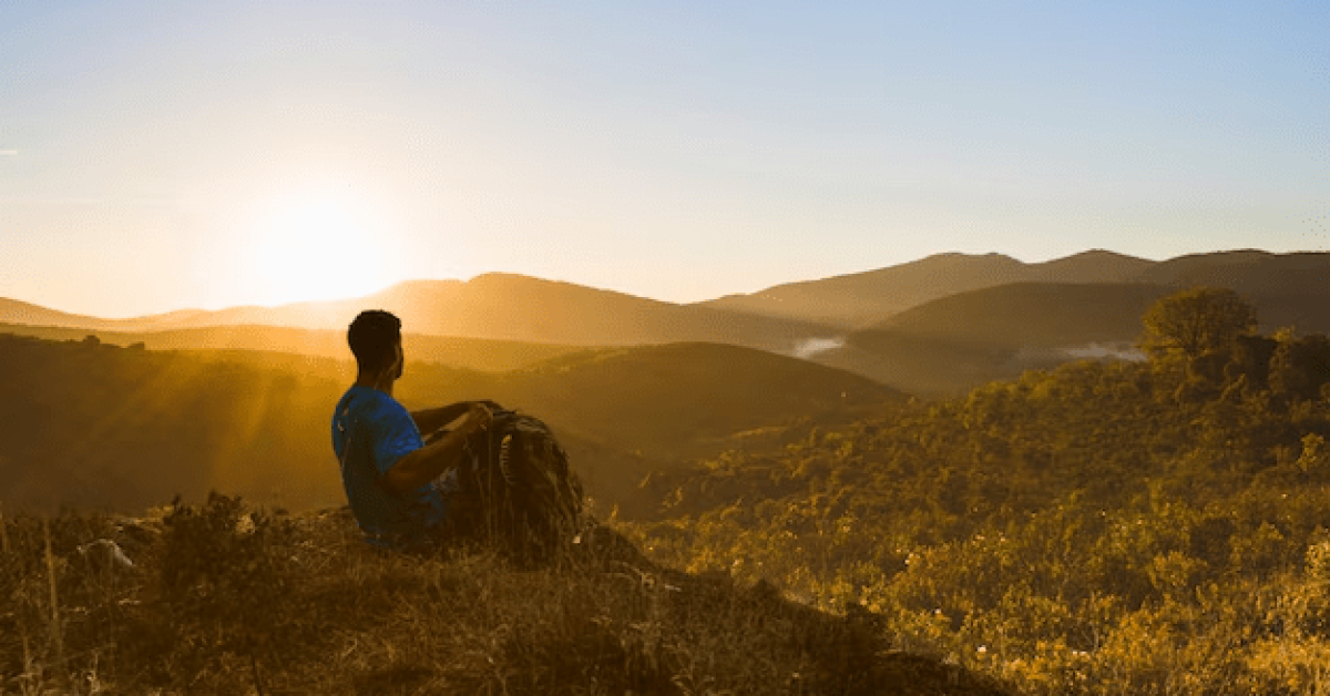 Person practicing yoga at sunrise on a mountain, embodying wellness travel and mindfulness vacations for self-care and recovery.
