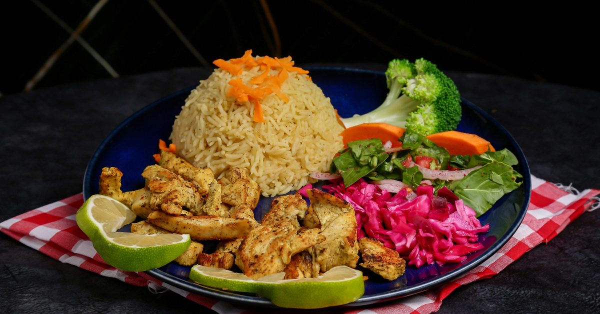 A plate with grilled chicken, seasoned rice, steamed broccoli, pickled cabbage, and lime wedges, representing nutrition in addiction recovery.