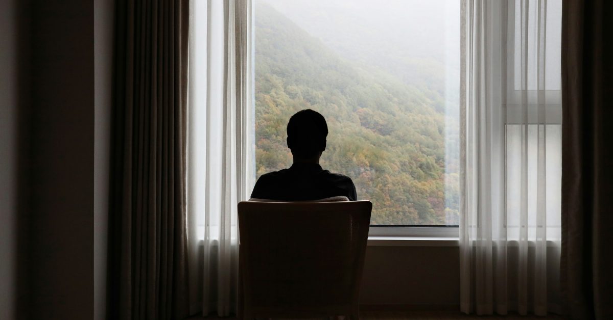 Person gazing out window toward misty hills, quietly asking themselves: do I need rehab and a fresh start.