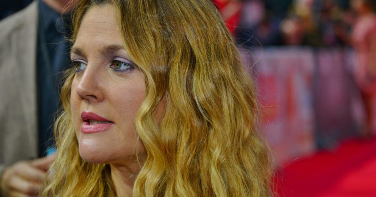 A close-up photograph of actress and producer Drew Barrymore on the red carpet for the movie Blended in Berlin. She has long, wavy blonde hair, light pink lipstick, and soft purple eyeshadow, looking slightly off-camera.