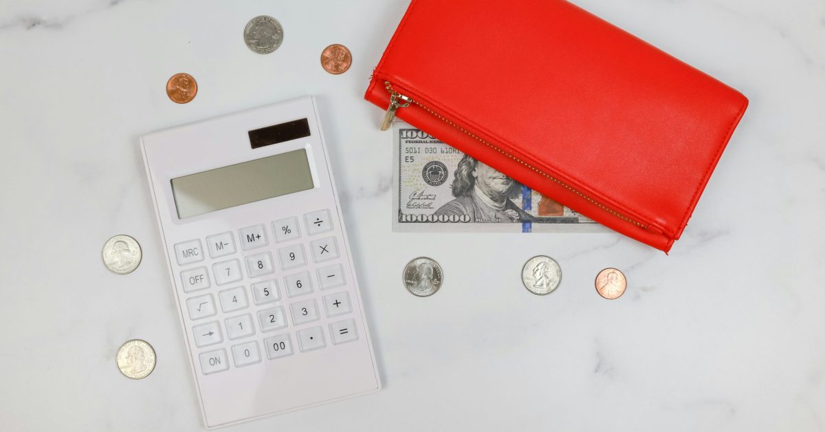 White calculator, red wallet, and scattered coins on a white surface, representing budgeting and smart money management after addiction recovery