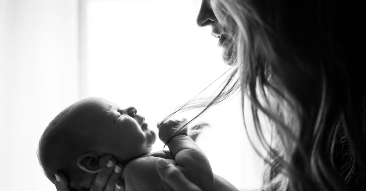 A thoughtful mother holding her baby near a window, symbolizing support and awareness during Maternal Mental Health Awareness Week.