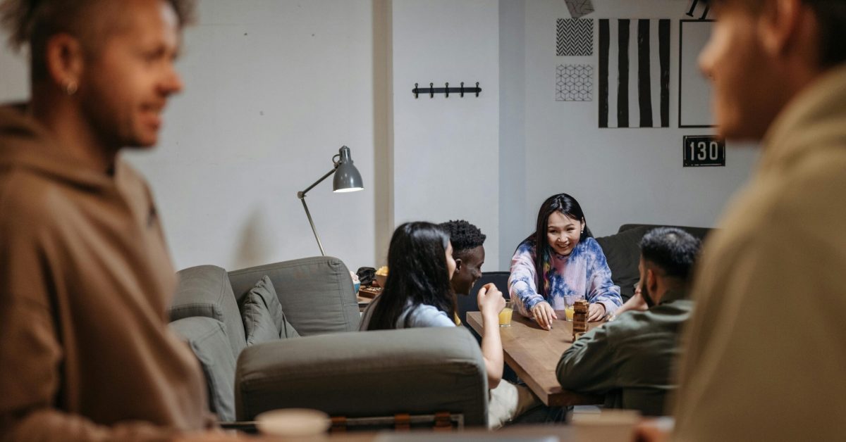 A diverse group of young adults sitting around a table, smiling and talking in a warm, supportive setting.