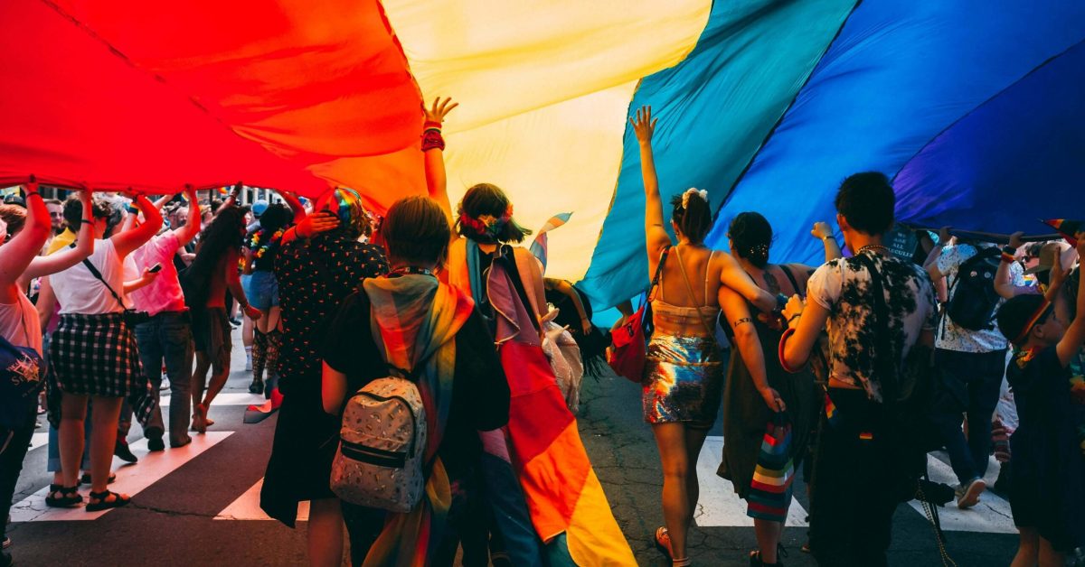 People celebrating under a giant rainbow flag during a Pride parade, symbolizing community and support during Pride Month