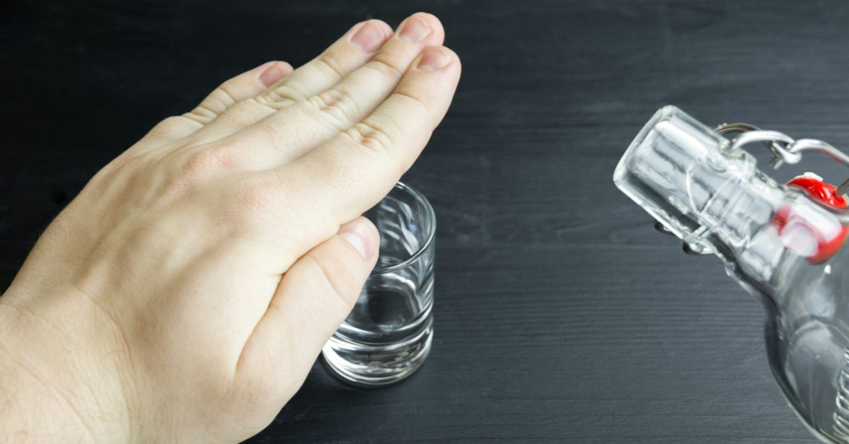 A person covering a shot glass with their hand to refuse alcohol, symbolizing understanding alcohol addiction and the decision to recover.